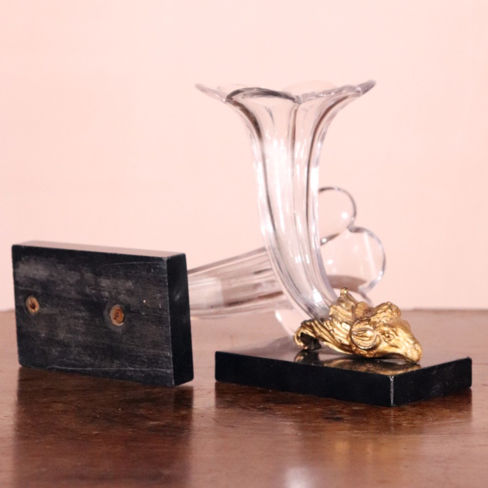 A pair of Regency cornucopia vases featuring fluted clear glass horns set into gilt bronze rams head mounts on rectangular black marble bases. View V