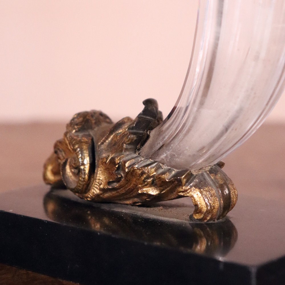 A pair of Regency cornucopia vases featuring fluted clear glass horns set into gilt bronze rams head mounts on rectangular black marble bases. View VI