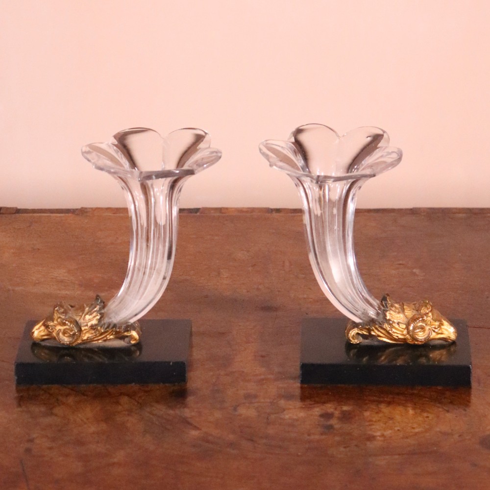 A pair of Regency cornucopia vases featuring fluted clear glass horns set into gilt bronze rams head mounts on rectangular black marble bases. View VII