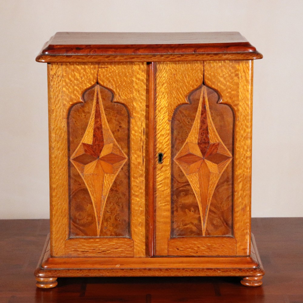 A 19th-century wooden table cabinet with two doors featuring inlaid star motifs set within pointed arches, resting on turned bun feet.