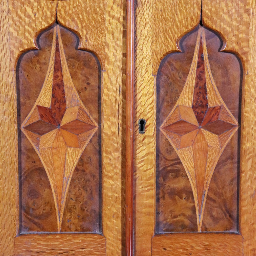 A 19th-century wooden table cabinet with two doors featuring inlaid star motifs set within pointed arches, resting on turned bun feet. View II