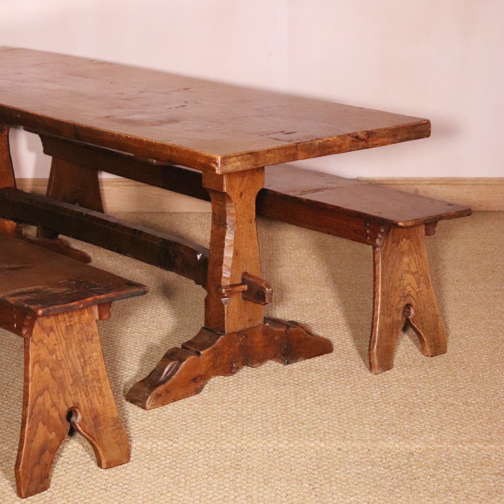 A handcrafted oak trestle dining table featuring an adzed tabletop, keyed stretcher joint, and two matching solid oak benches.