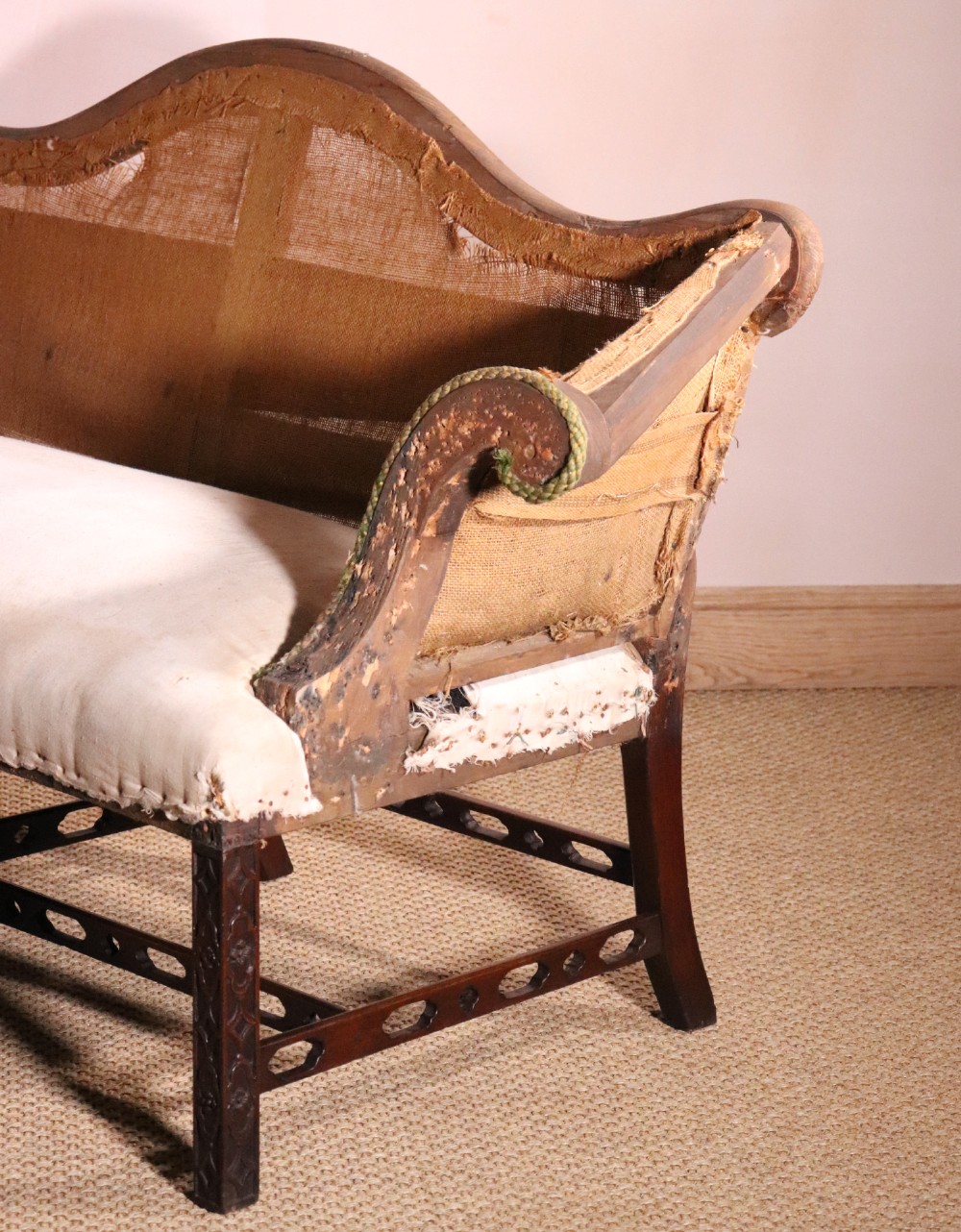 An antique Chippendale style mahogany settee featuring a serpentine camel back, scrolled arms, pierced stretchers, and exposed base lining fabric. View IV