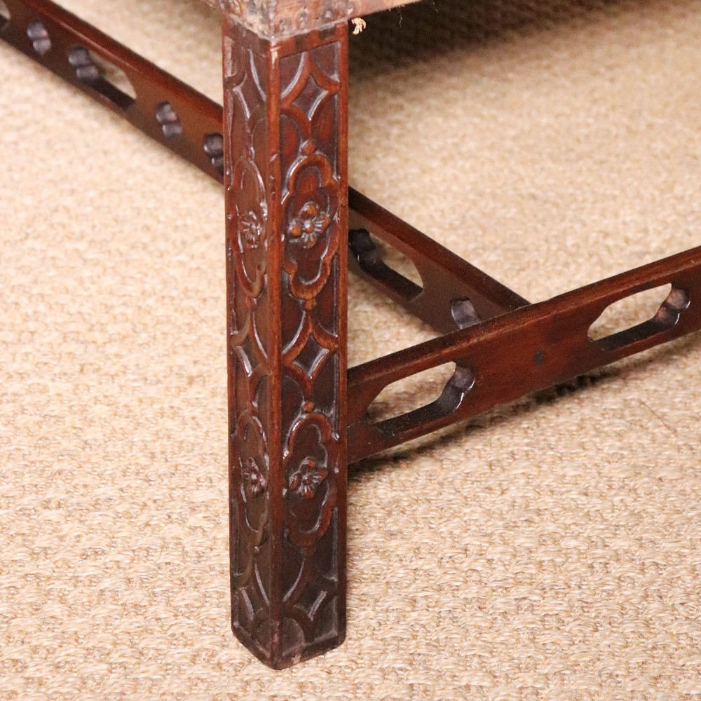 An antique Chippendale style mahogany settee featuring a serpentine camel back, scrolled arms, pierced stretchers, and exposed base lining fabric. View V