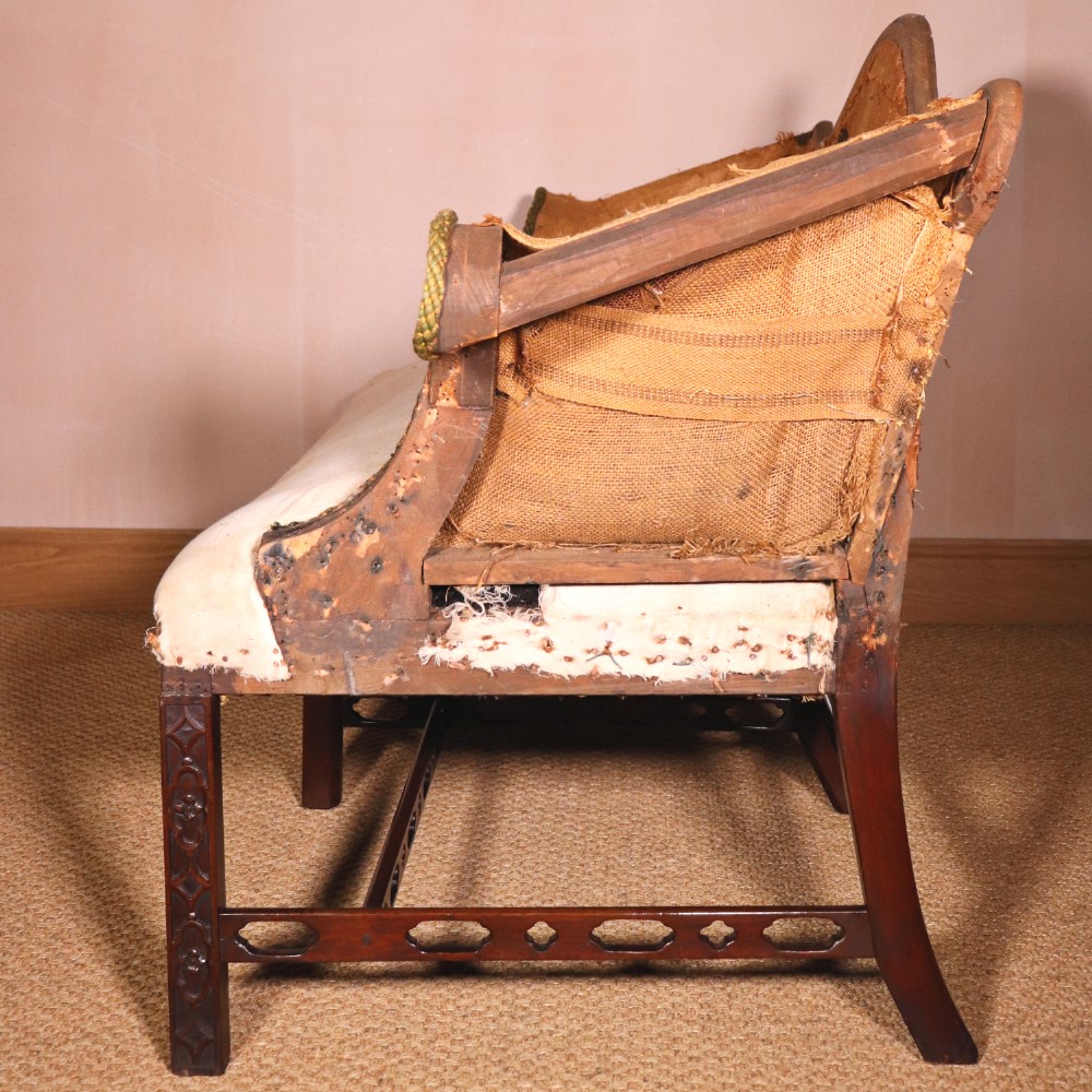 An antique Chippendale style mahogany settee featuring a serpentine camel back, scrolled arms, pierced stretchers, and exposed base lining fabric. View VII