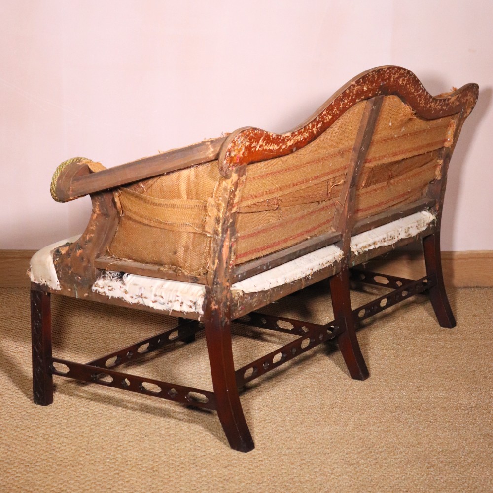 An antique Chippendale style mahogany settee featuring a serpentine camel back, scrolled arms, pierced stretchers, and exposed base lining fabric. View VIII