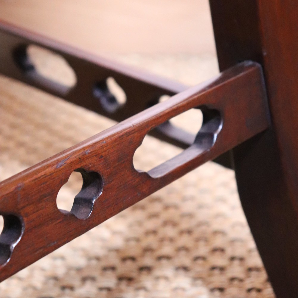 An antique Chippendale style mahogany settee featuring a serpentine camel back, scrolled arms, pierced stretchers, and exposed base lining fabric. View IX