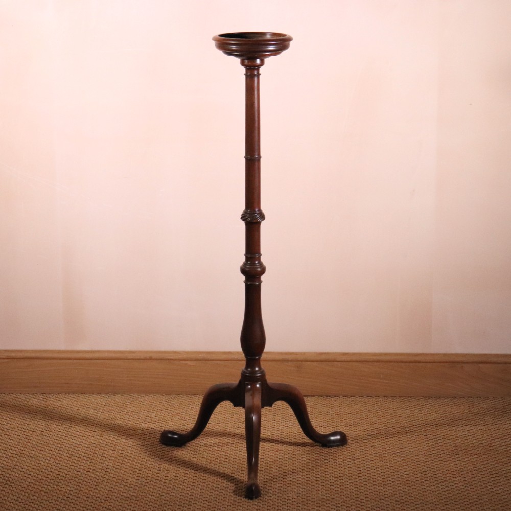 A George II dark mahogany torchere featuring a dished top, turned baluster column, and a tripod base with pad feet.
