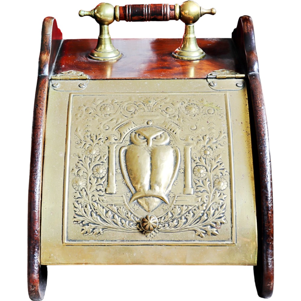 An Arts and Crafts mahogany coal scuttle featuring a sloped brass lid embossed with an owl design and a turned top handle.