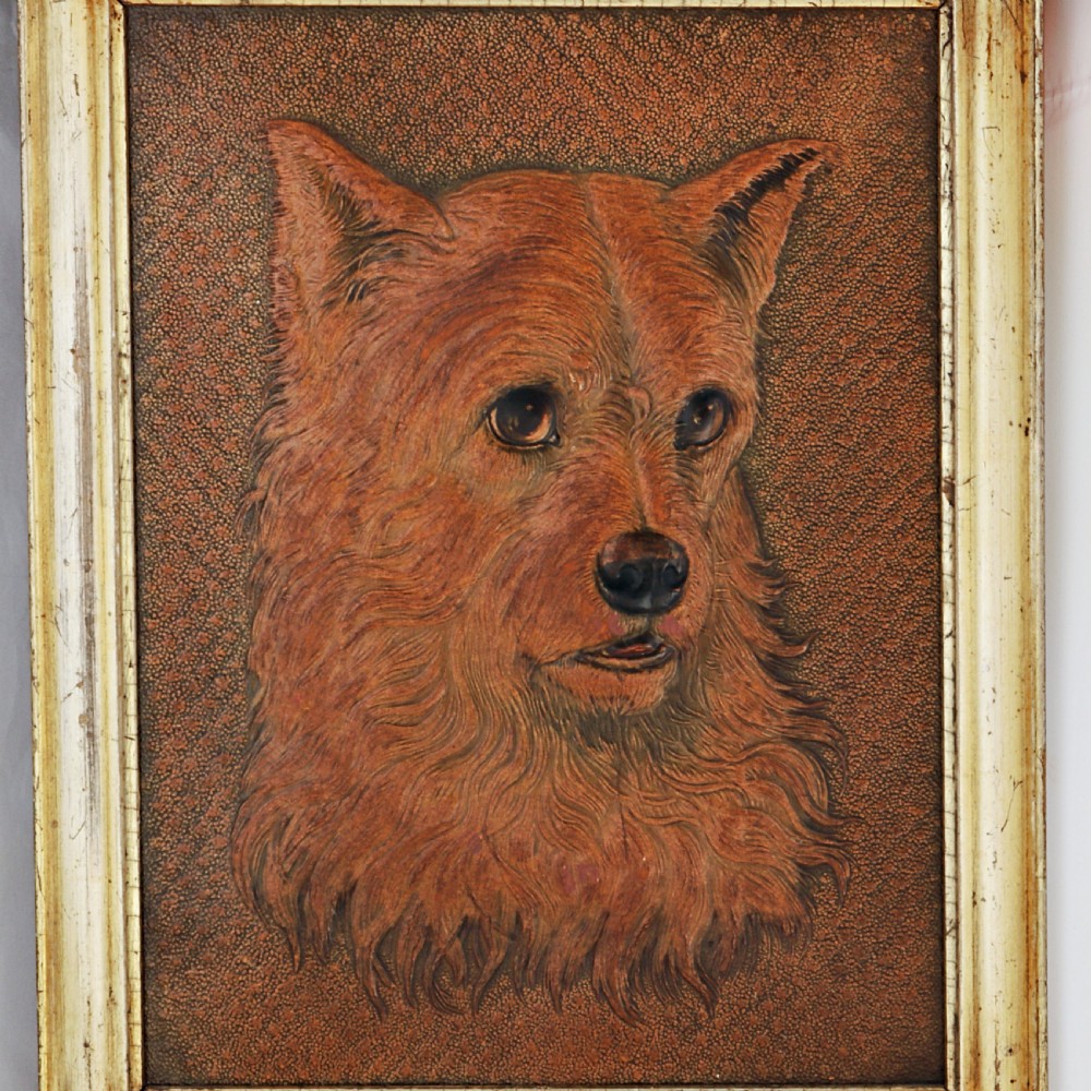 A framed embossed leather panel depicting the three-dimensional head of a terrier dog within a textured background and a pale gilt wooden frame. View II