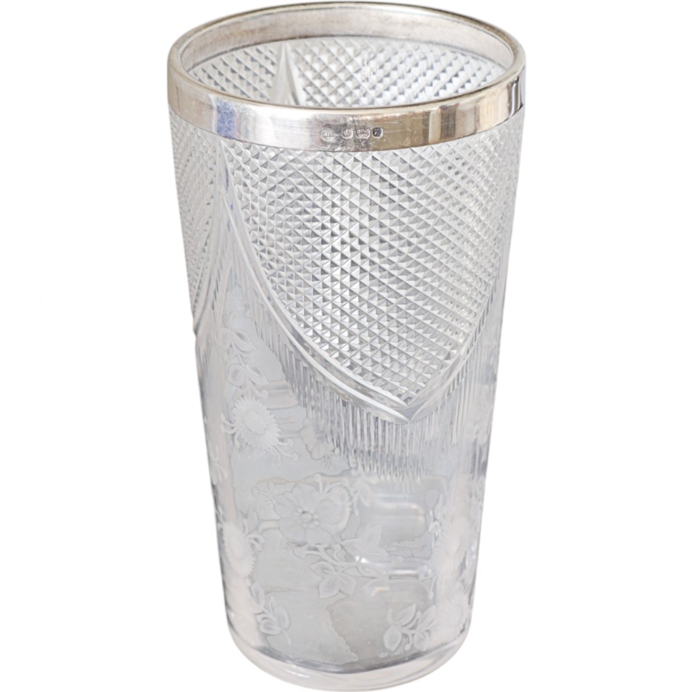 A cylindrical clear cut glass vase featuring diamond geometric patterns, etched floral motifs, and a polished sterling silver rim with visible hallmarks.