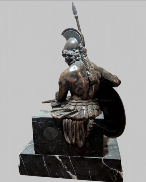 fig 1. A 19th-century bronze sculpture depicting the mythological Greek warrior Ajax seated with a helmet, spear, and decorated shield on a black marble base.