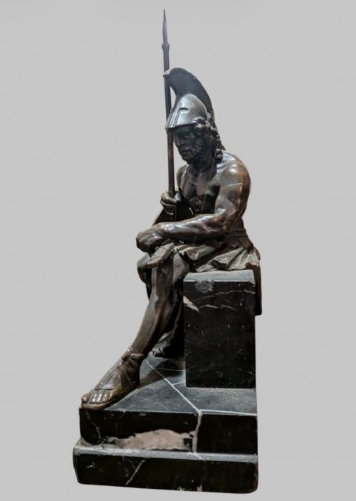 fig 2. A 19th-century bronze sculpture depicting the mythological Greek warrior Ajax seated with a helmet, spear, and decorated shield on a black marble base.