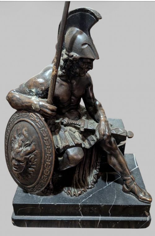 fig 3. A 19th-century bronze sculpture depicting the mythological Greek warrior Ajax seated with a helmet, spear, and decorated shield on a black marble base.
