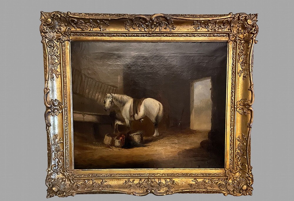 An antique oil painting depicting a white horse inside a stable, framed in an ornate gilded wood frame.