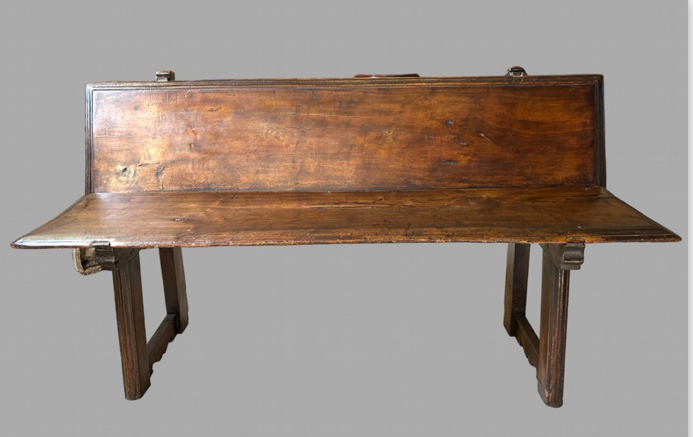 A dark brown wooden bench with a high solid backrest, flat seat, and straight trestle supports.