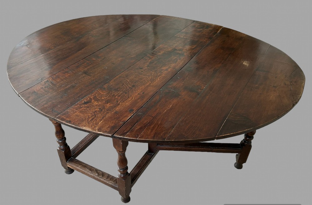 An overhead angled view of a large, dark brown antique oak gateleg table with turned legs and multiple drop leaves fully extended.