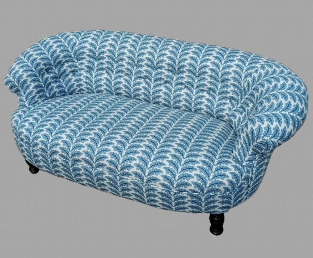 A Victorian button-back sofa upholstered in a blue and white patterned fabric with turned dark wooden legs.