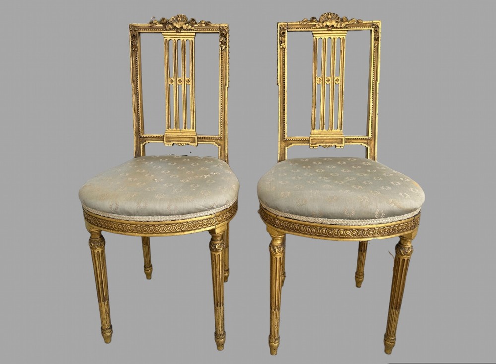 A pair of French Empire period giltwood salon chairs with fluted legs, carved backrests, and pale blue patterned upholstered seats.