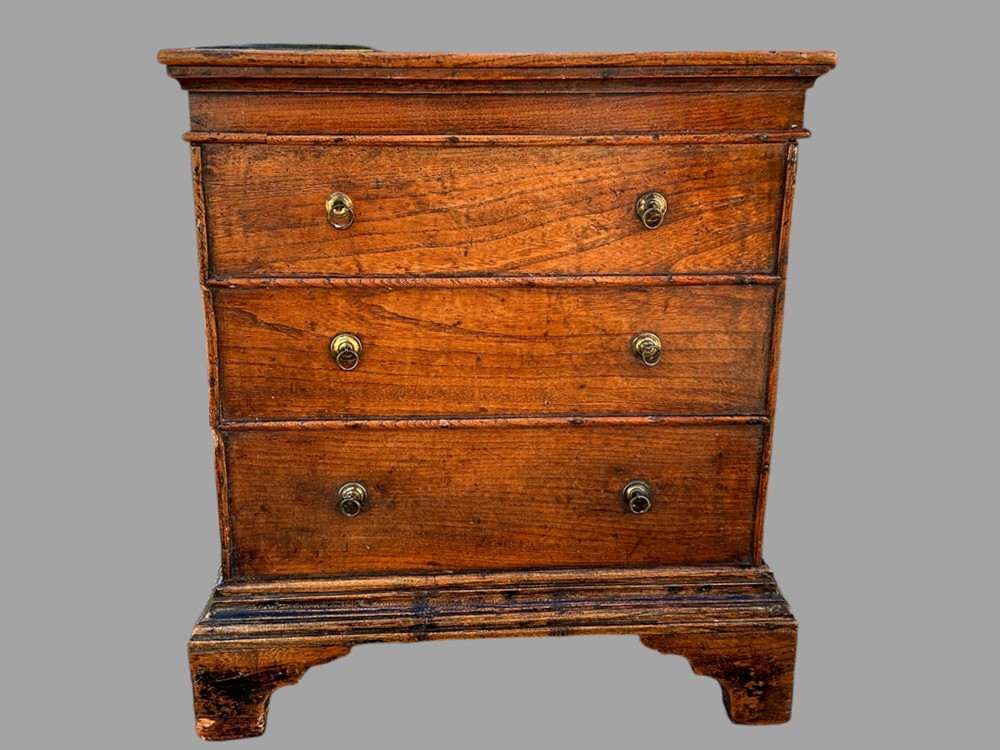 A 19th-century warm brown elm commode chest featuring three drawers with brass ring handles, raised on shaped bracket feet.