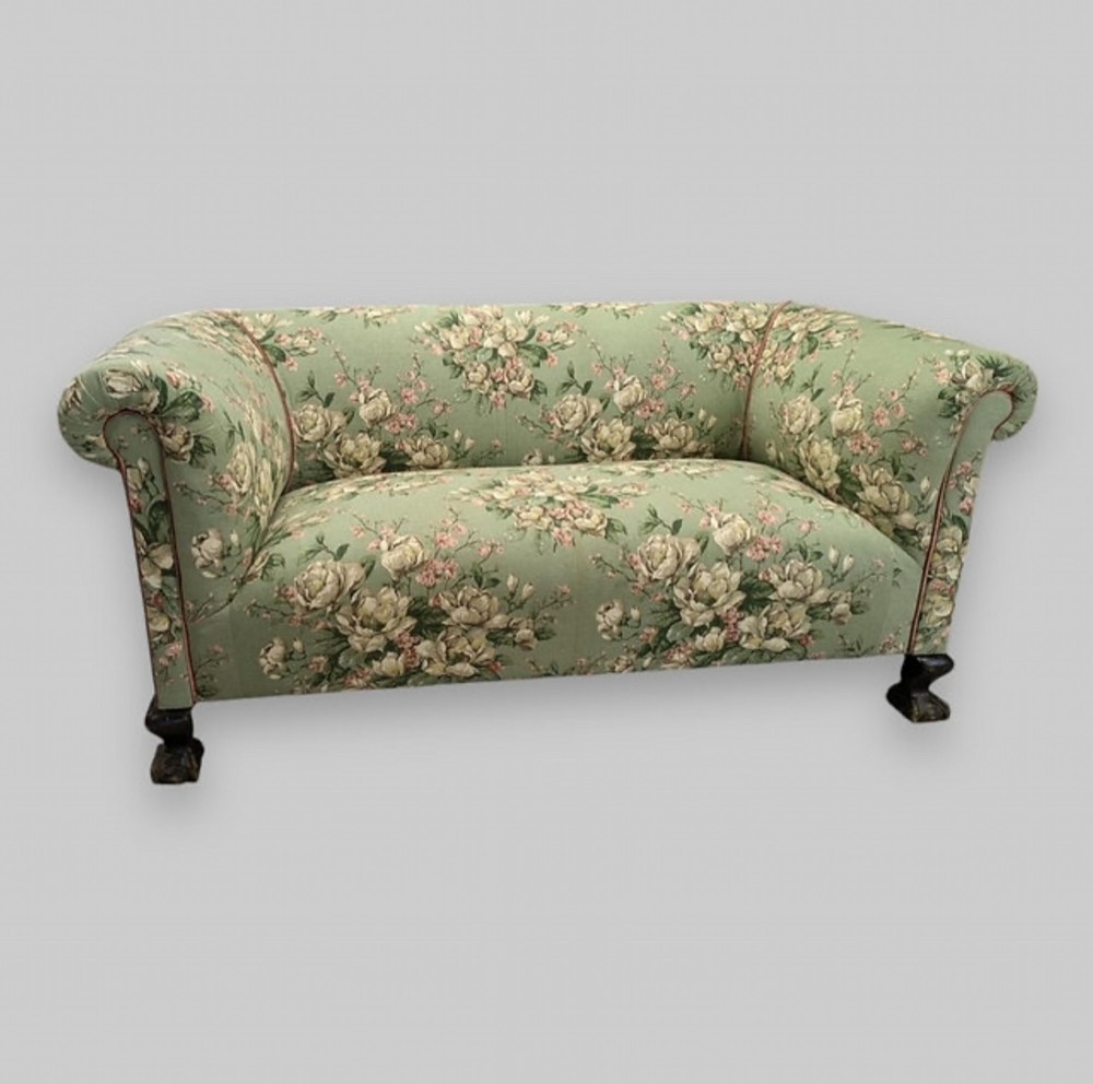 An Edwardian chesterfield sofa upholstered in sage green floral fabric with dark carved wood feet.