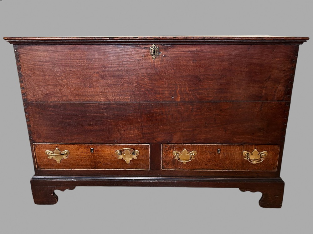 An antique dark oak mule chest featuring a lift-top lid above two lower drawers fitted with brass drop handles and bracket feet.