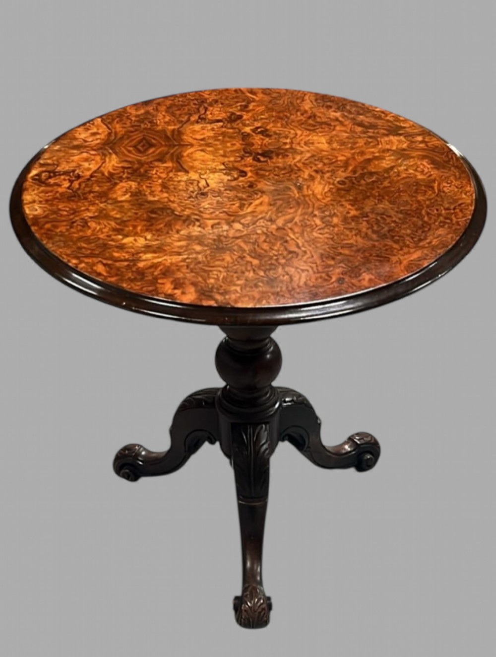 A round occasional table featuring a highly figured burr walnut veneer top resting on a turned central stem and a carved tripod base.