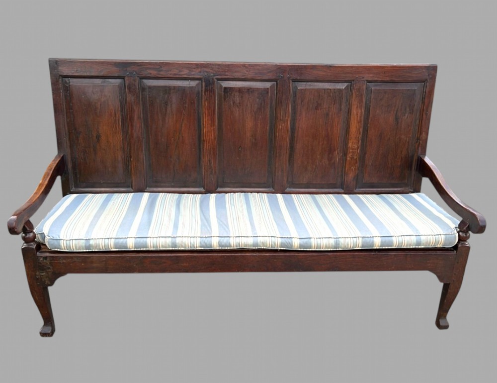 An 18th-century Georgian dark oak settle featuring a five-panel high back, curved armrests, cabriole legs, and a striped blue cushion.