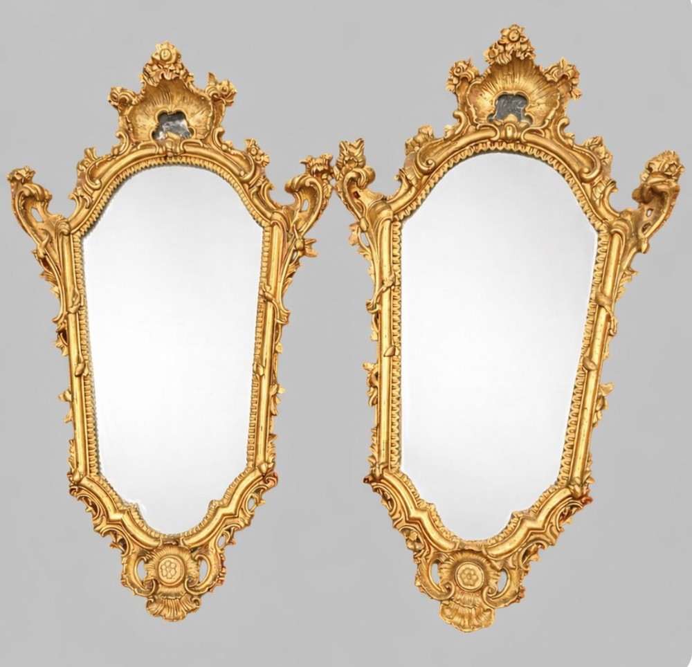 A pair of early twentieth-century giltwood wall mirrors crafted in the Louis XV manner with carved rocaille crestings, asymmetrical C-scroll borders, and shaped glass plates.