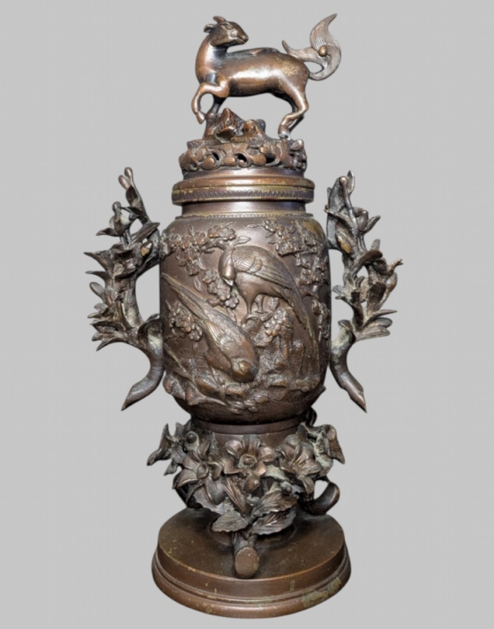 An antique cast bronze Japanese incense burner featuring a goat finial, foliage handles, bird relief panels, and a stepped circular base.