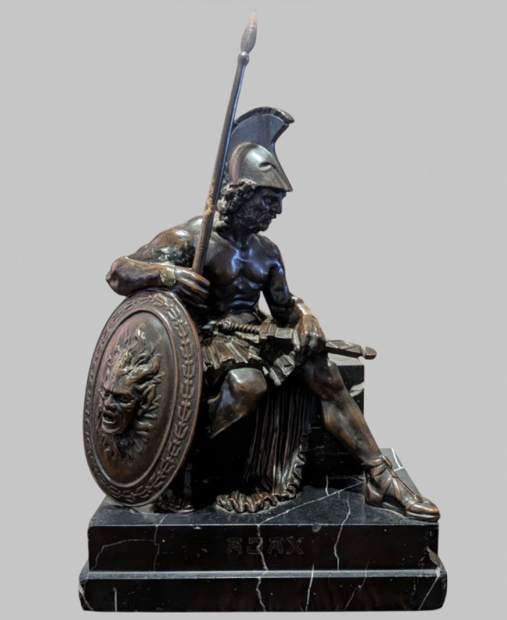 A 19th-century bronze sculpture depicting the mythological Greek warrior Ajax seated with a helmet, spear, and decorated shield on a black marble base.
