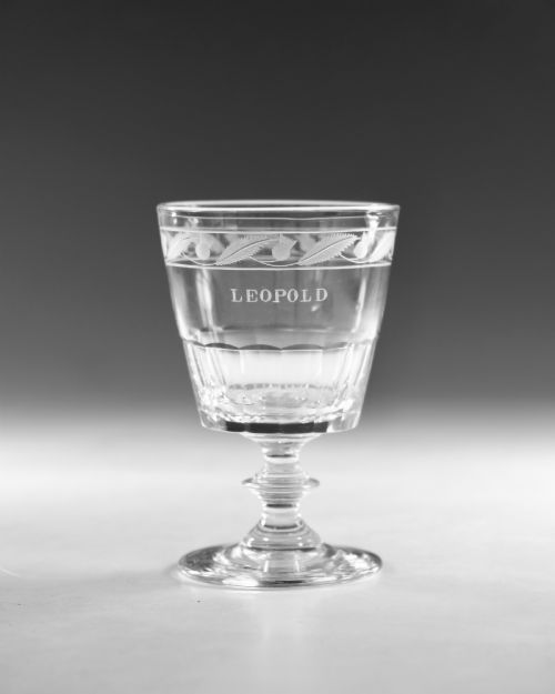 fig 1. A clear Georgian lead crystal rummer glass featuring an engraved inscription reading LEOPOLD above a facet-cut lower bowl and knopped stem.