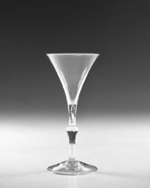 fig 1. An 18th-century clear glass Georgian wine glass featuring a flared trumpet bowl, a knopped stem with an internal air teardrop inclusion, and a wide circular foot.