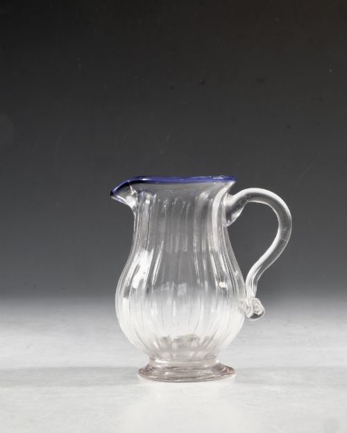 fig 1. An English Georgian blown clear glass cream jug featuring vertical fluting, a loop handle, and an applied cobalt blue rim.
