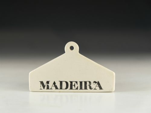 fig 1. A mid-19th-century white ceramic wine bin label with a top mounting hole, printed with the text MADEIRA in black capital letters.