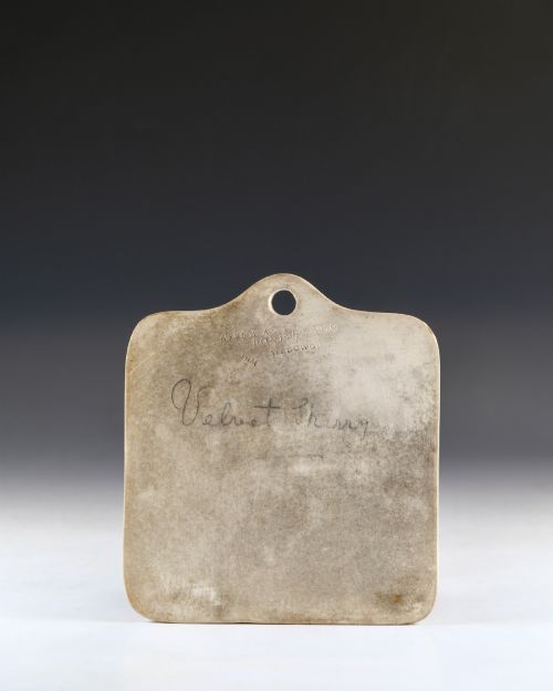 fig 1. An off-white ceramic wine cellar bin label featuring an arched top with a central hanging hole, impressed maker marks, and cursive writing reading Velvet Sherry.