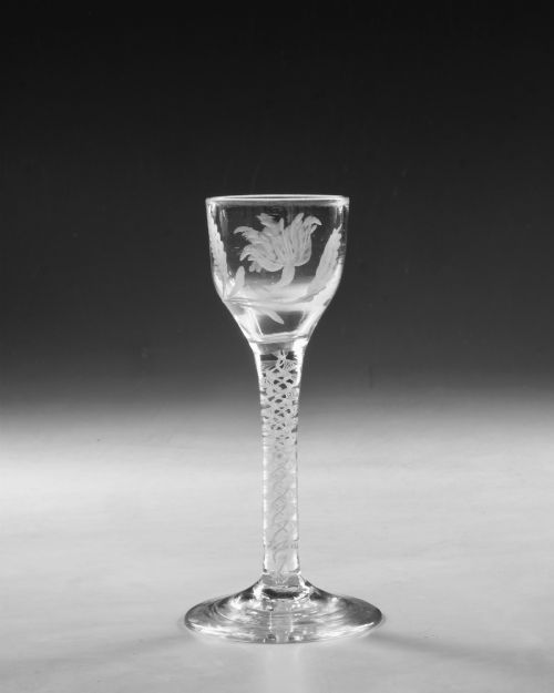 fig 1. An 18th-century Georgian clear glass wine goblet featuring a wheel-engraved floral bowl, an internal opaque white twist stem, and a flat conical base.