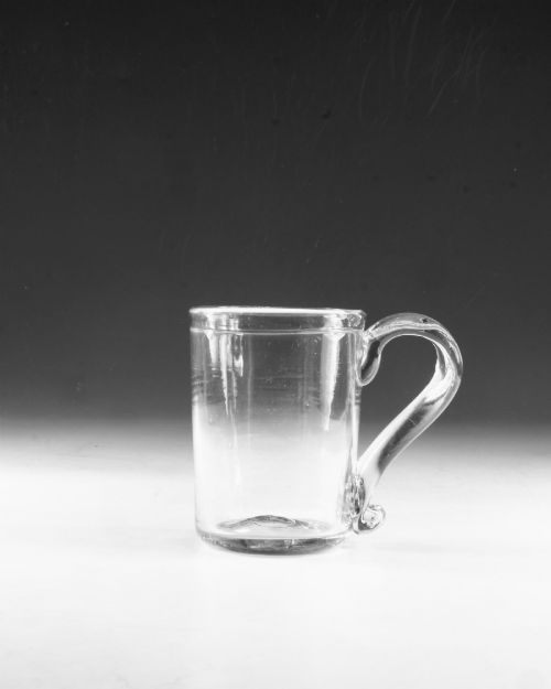 fig 1. An 18th-century clear glass tankard featuring a cylindrical body and a curved strap handle with a scrolled lower terminal.