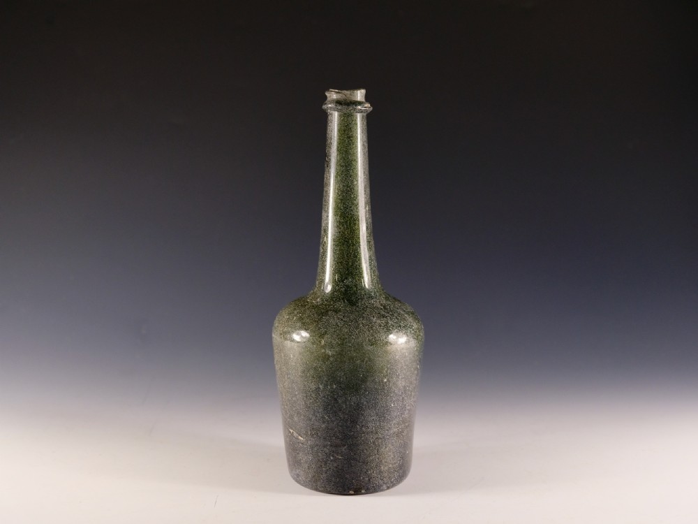 An 18th-century hand-blown dark olive green glass Calvados bottle featuring a long tapered neck with an applied string rim.