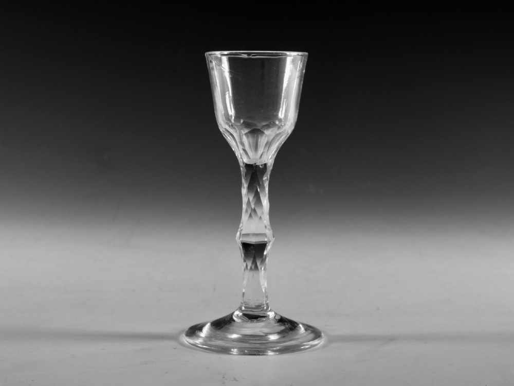 An eighteenth-century clear lead glass wine glass featuring a diamond facet-cut stem and a conical bowl resting on a flat circular foot.