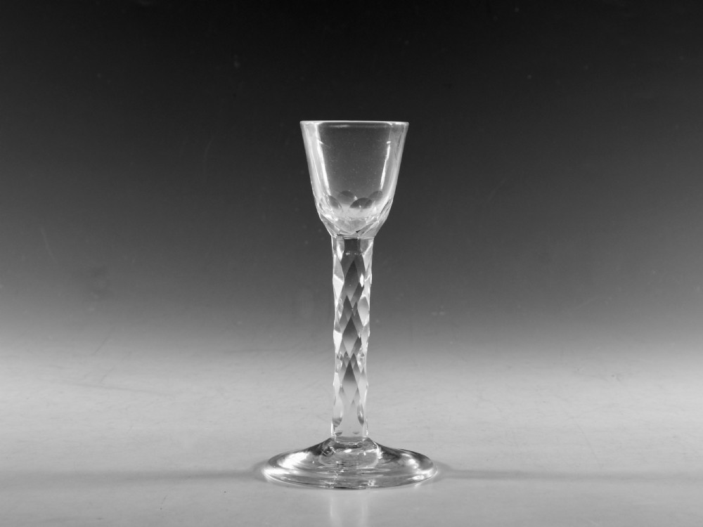 An 18th-century clear glass cordial glass featuring a small conical bowl, a geometric facet-cut stem, and a flat circular foot.