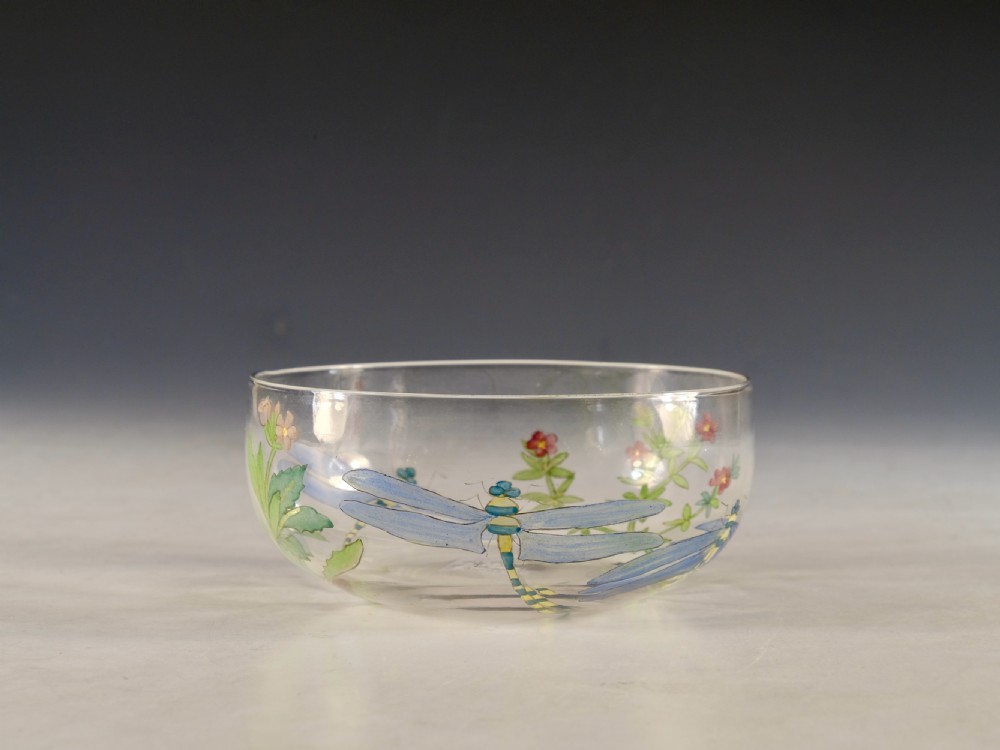 A clear circular glass finger bowl hand-painted with blue dragonflies, green foliage, and small red flowers around the exterior surface.