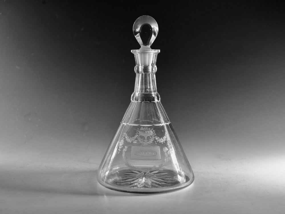 A clear Georgian cut glass ship decanter featuring a broad conical base, floral wheel engraving, a ringed neck, and a loop stopper.