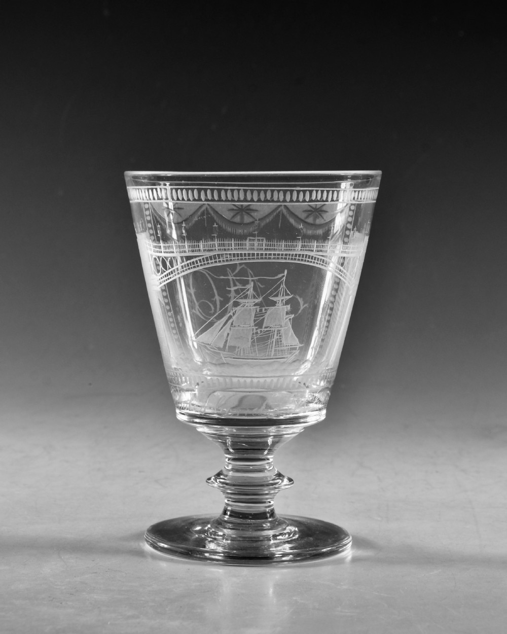 An antique clear lead glass rummer featuring detailed wheel engraving of a sailing ship beneath a bridge, set on a knopped stem and circular foot. View II