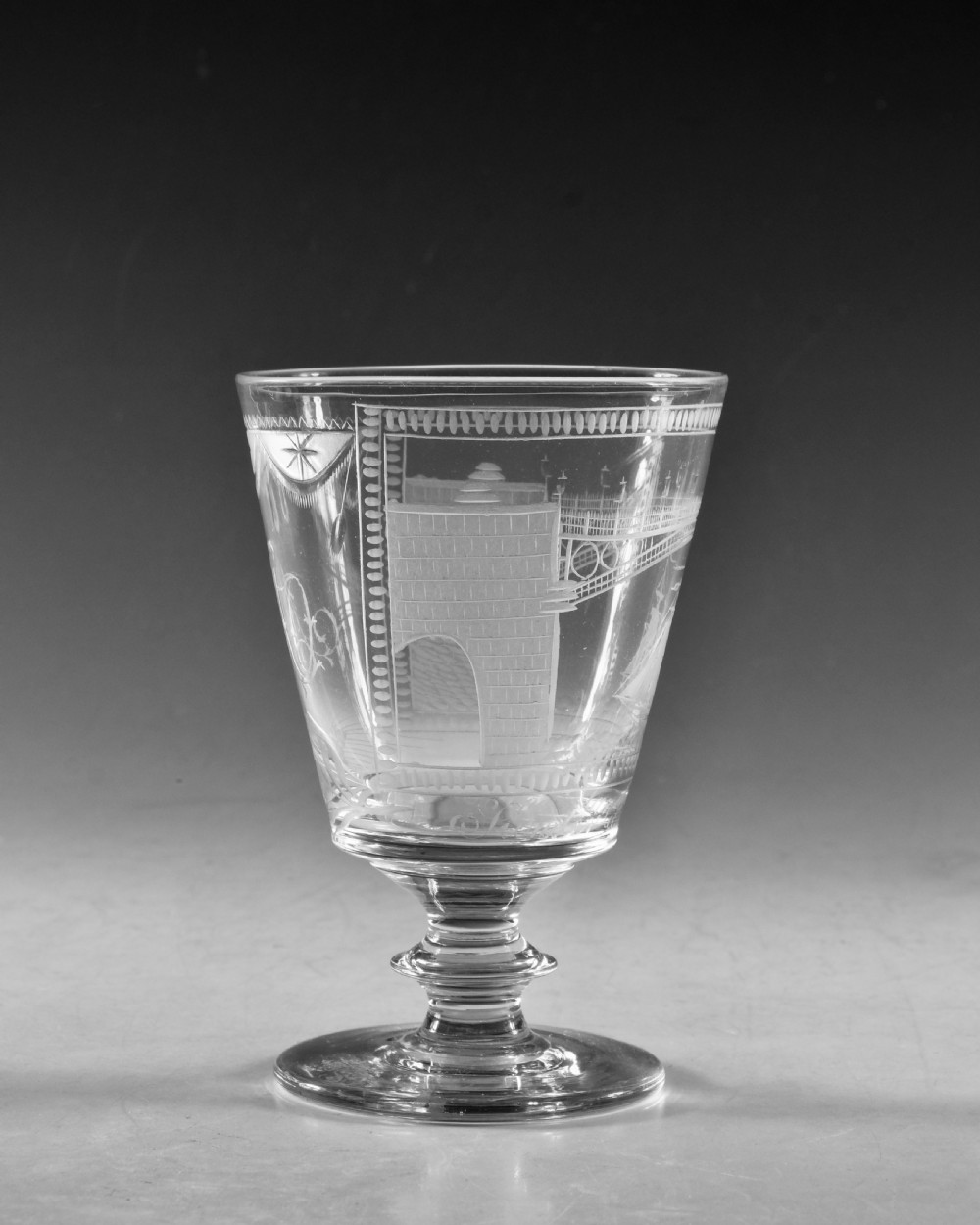 An antique clear lead glass rummer featuring detailed wheel engraving of a sailing ship beneath a bridge, set on a knopped stem and circular foot. View III