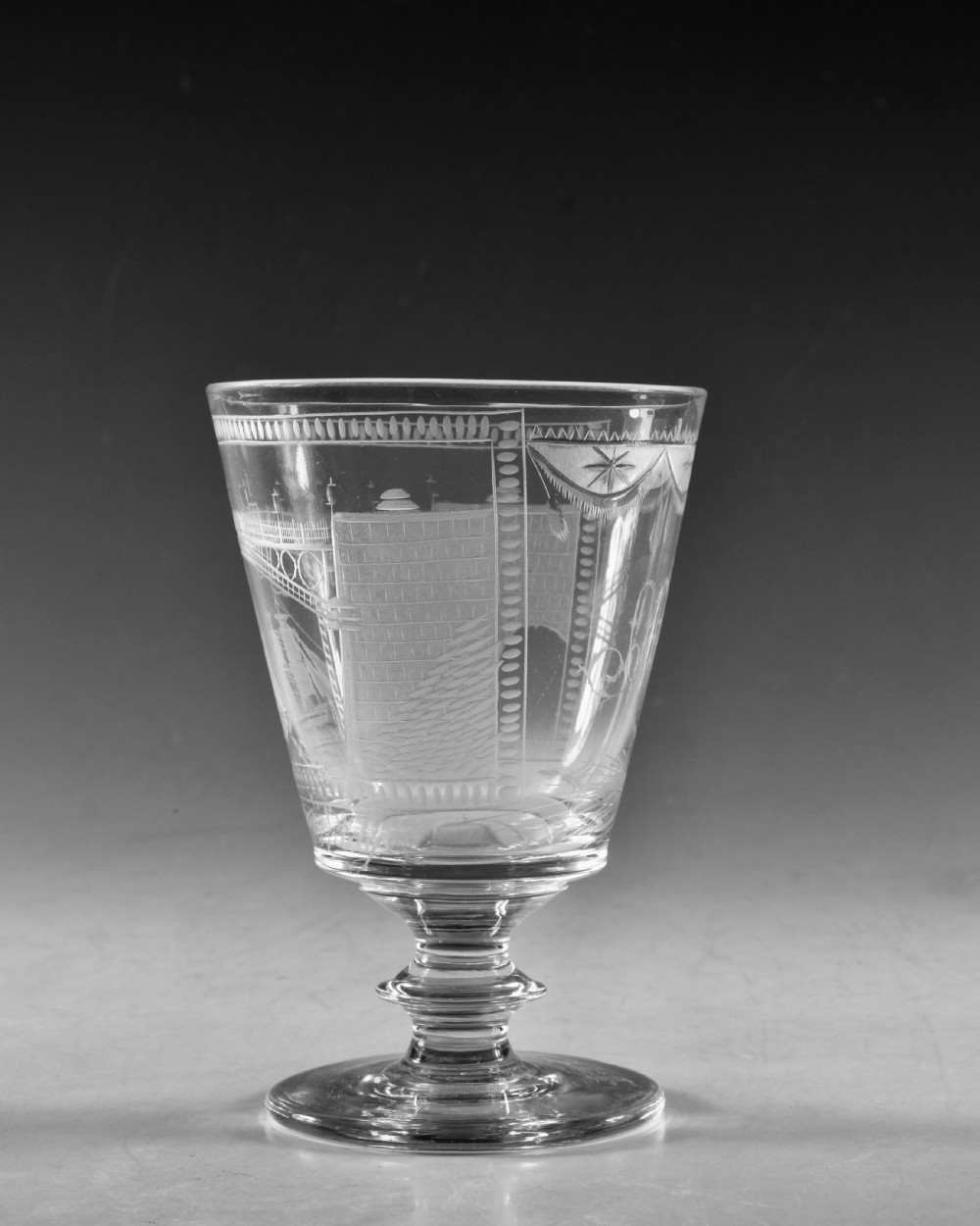 An antique clear lead glass rummer featuring detailed wheel engraving of a sailing ship beneath a bridge, set on a knopped stem and circular foot. View V