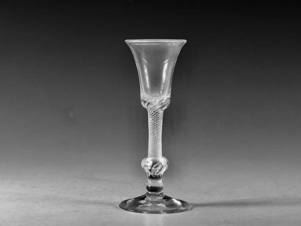 An 18th-century clear glass wine goblet featuring a flared bell bowl resting on a composite stem with internal twist decoration and a conical flat foot.