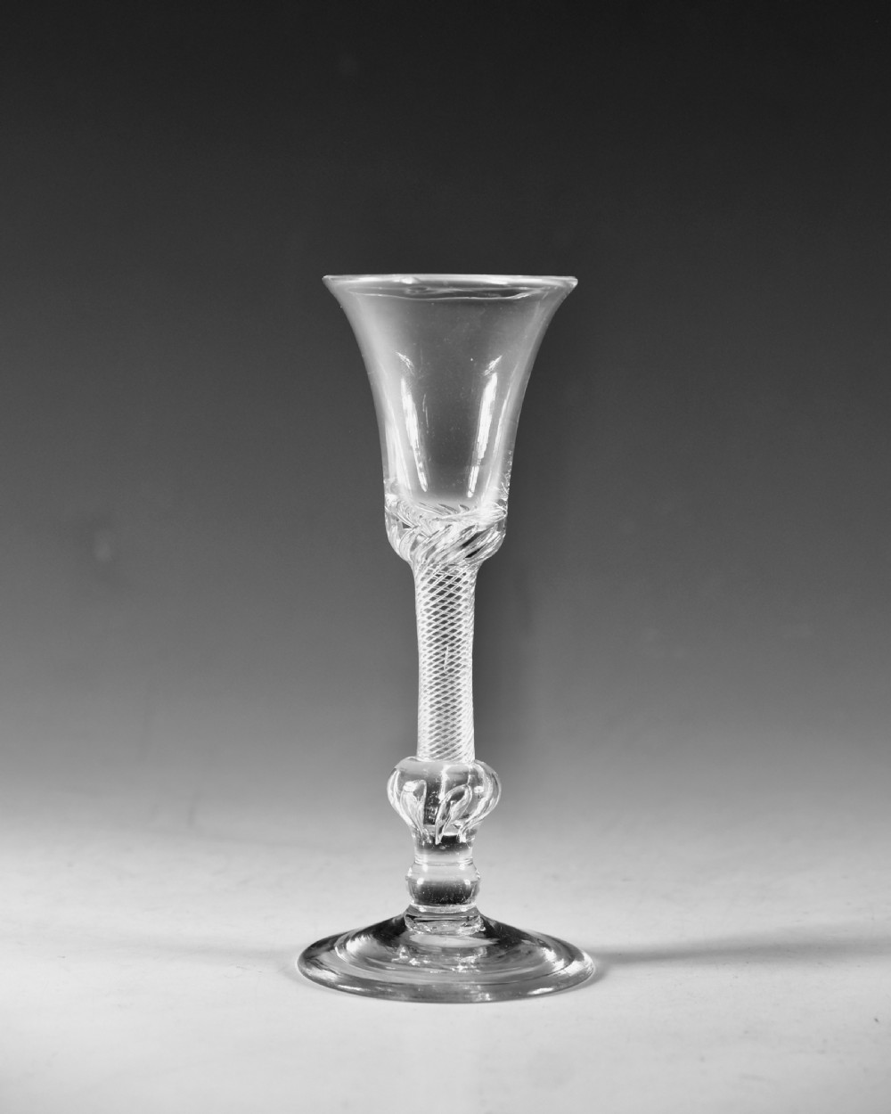 An 18th-century clear glass wine goblet featuring a flared bell bowl resting on a composite stem with internal twist decoration and a conical flat foot. View II
