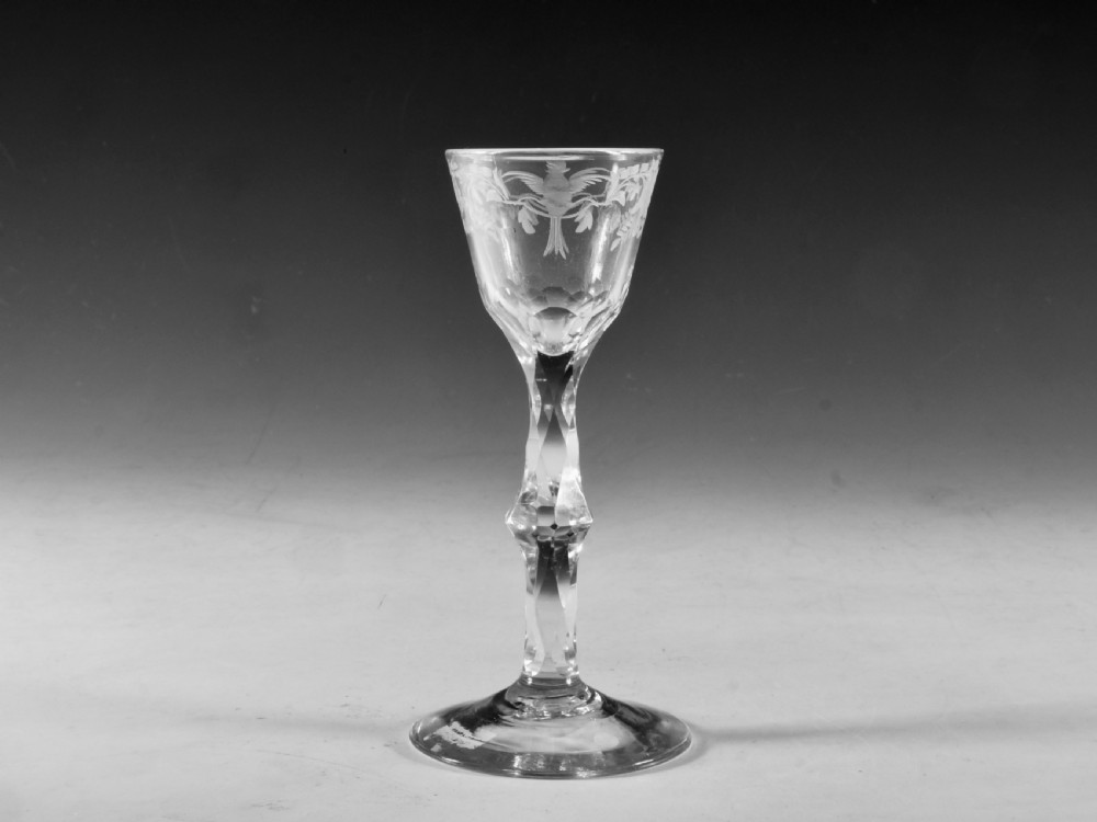 An 18th-century clear glass wine goblet featuring a wheel-engraved bird motif on the rounded bowl and a diamond-facet cut stem resting on a flat circular base.