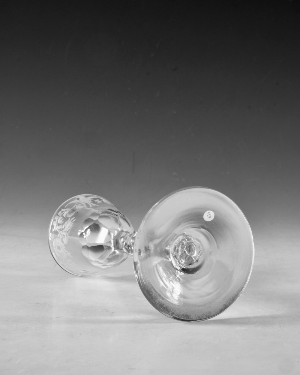 An 18th-century clear glass wine goblet featuring a wheel-engraved bird motif on the rounded bowl and a diamond-facet cut stem resting on a flat circular base. View V